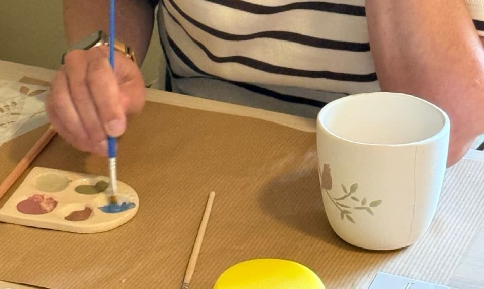 Een deelnemer mengt glazuur en beschildert een witte keramieken mok
