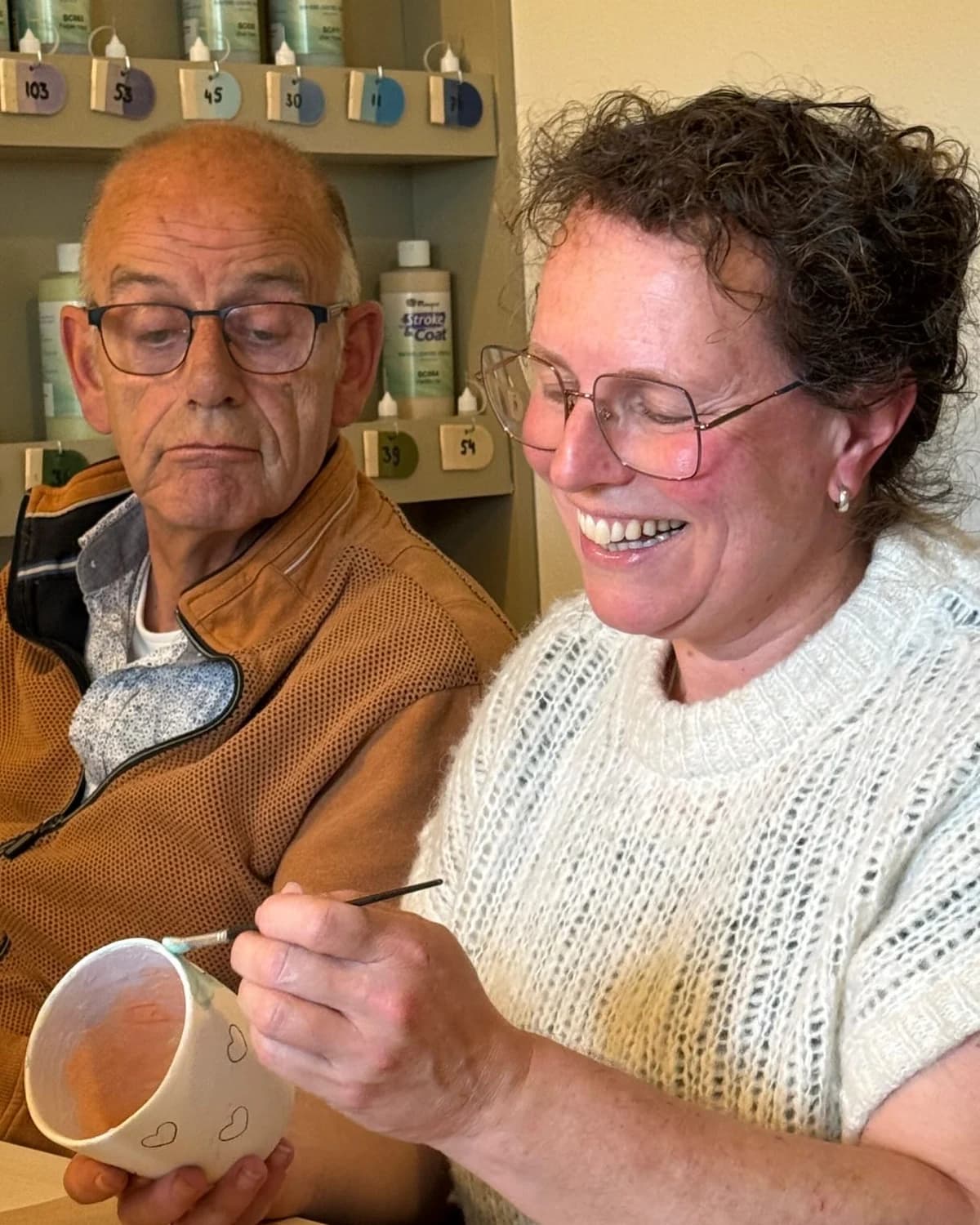 Een deelnemer beschildert glimlachend een keramieken mok in het atelier